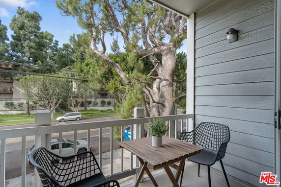 View from a balcony with two chairs and a table overlooking the street and trees.