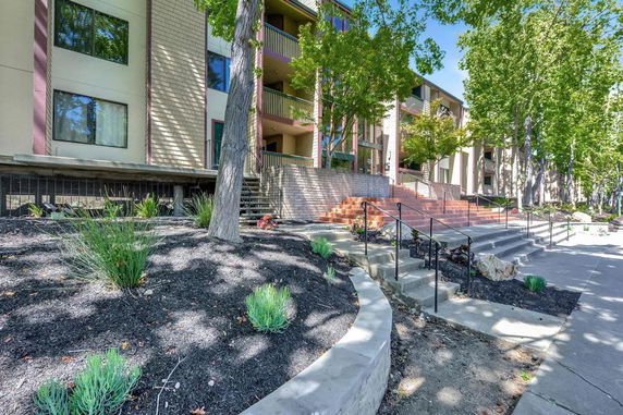 Front view of a multi-story apartment building with stairs and mature trees.