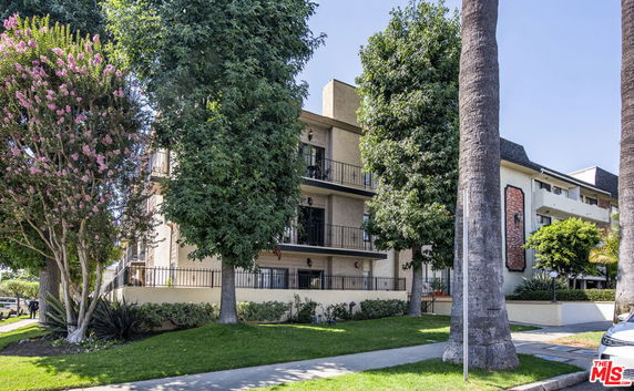 Front view of a multi-story building with balconies surrounded by trees.