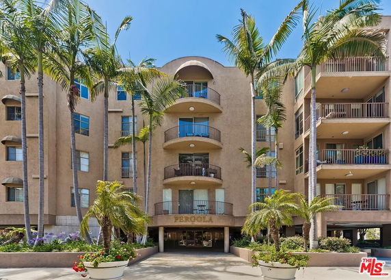 Front view of a multi-story building with balconies and palm trees.