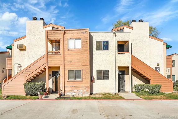 Front view of a two-story residential building with multiple apartments and exterior staircases leading to the upper floor.