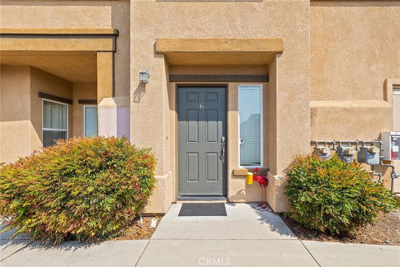 Front view of a house entrance with a grey door and surrounding plants.