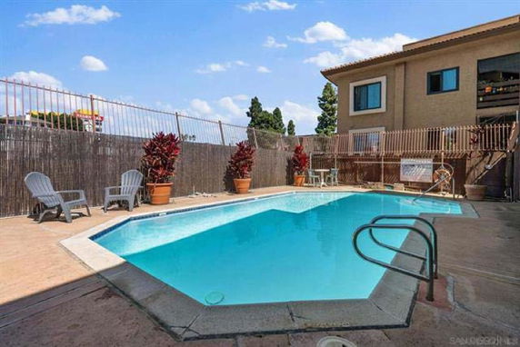 Outdoor swimming pool adjacent to a building with chairs and potted plants around it.