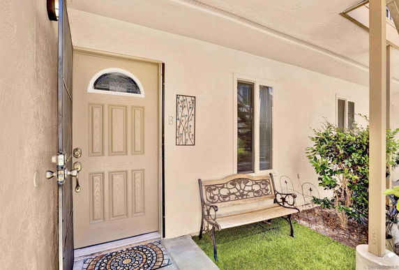 Front view of a house entrance with a wooden door, windows, and a bench outside.
