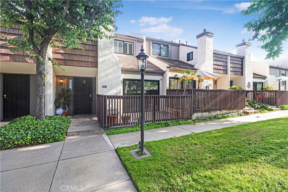 Front view of a townhouse with a small fenced patio and two chimneys.