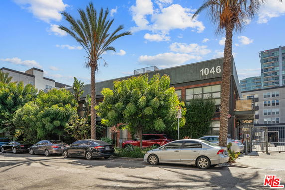 Front view of a commercial building with greenery and parked cars.