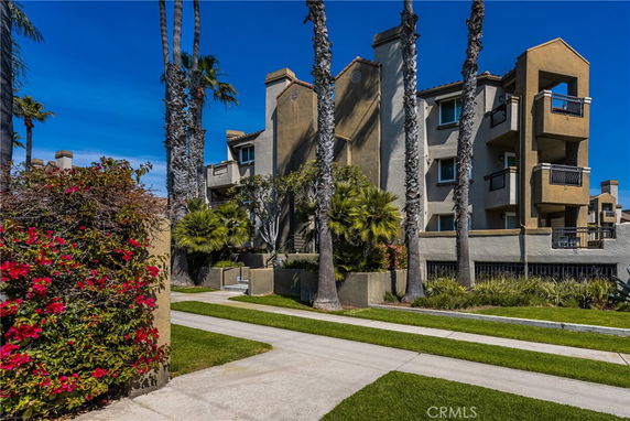 Front view of a multi-story residential building with balconies and palm trees in front.