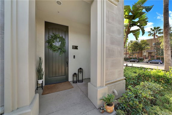 Front entrance of a house with a green door, potted plants, and decorative wreath.
