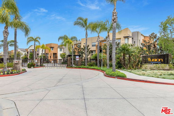 Front view of a housing complex entry with palm trees and sign.