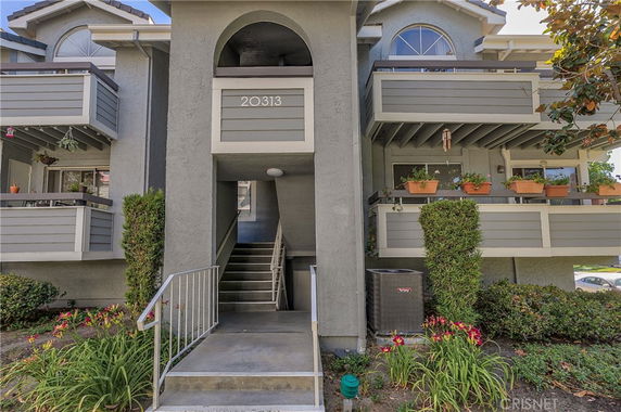 Front view of a multi-story residential building with balconies and a central stairway entrance.