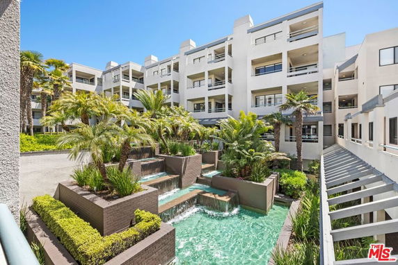 Front view of a multi-story residential building with palm trees and a water feature.