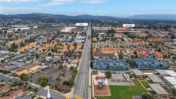 Aerial view of a suburban area with a main road, residential buildings, and a distant view of shopping centers.