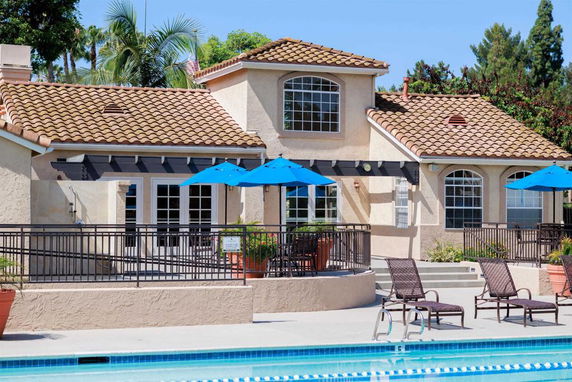 Front view of a house with a tiled roof and a swimming pool area featuring lounge chairs and umbrellas.