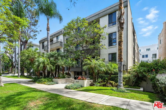 Front view of a multi-story residential building with balconies and surrounded by palm trees.
