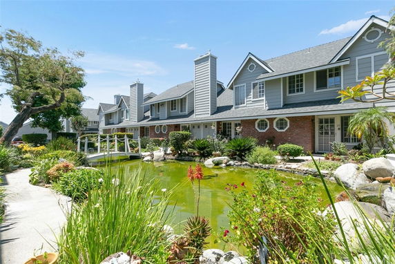 Front view of a two-story house with a pond and bridge in the foreground.