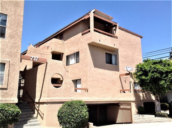 Front view of a multi-story building with beige stucco exterior and a recessed entrance.