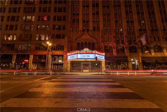 Front view of an ornate historic theater building with a marquee displaying messages, located at a crosswalk.