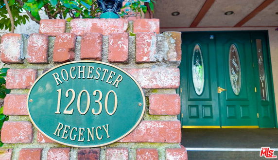 Entrance of a building with green double doors and a brick wall with a nameplate.
