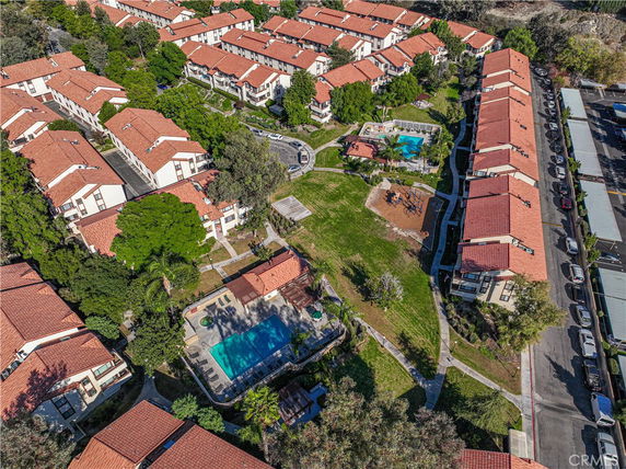 Aerial view of a residential complex with multiple buildings, a swimming pool, and surrounding greenery.