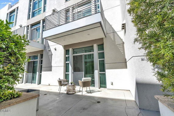 Front view of a modern multi-story building with balconies and a small outdoor seating area.