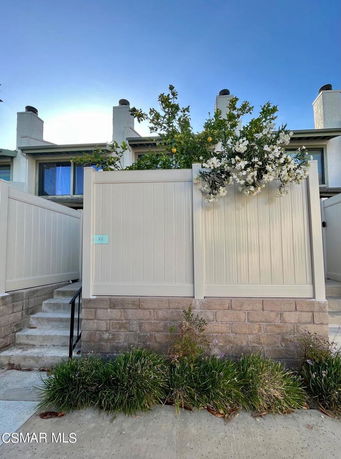 Front view of a multi-story townhouse with a white fence and brick base.