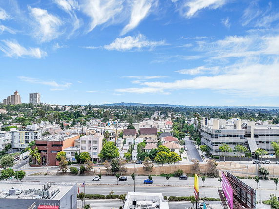 Panoramic view of a cityscape with buildings and distant hills under a blue sky.