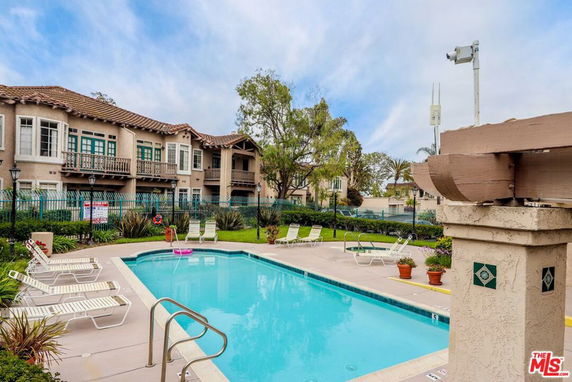 Outdoor swimming pool area with lounge chairs and nearby residential buildings.