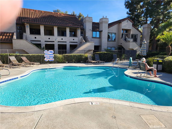 Outdoor view of a swimming pool in front of a residential building with deck chairs and umbrellas around.