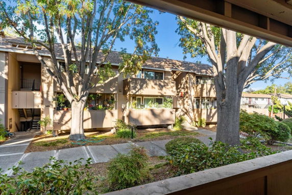Front view of a two-story residential building with balconies and surrounding trees.