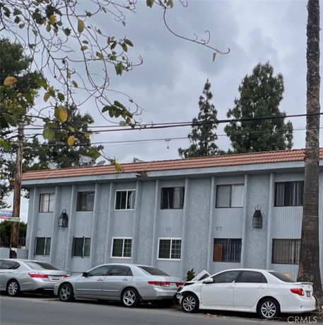 Front view of a two-story residential building with a tiled roof and multiple cars parked in front.