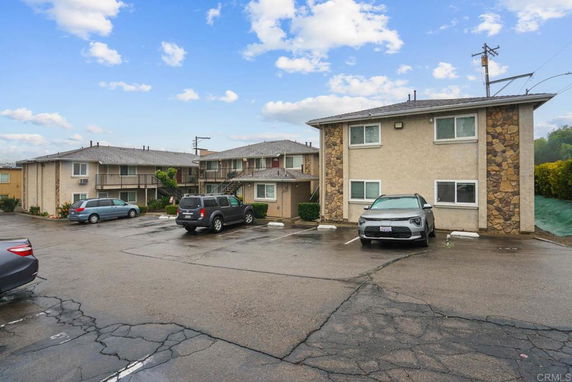 Outdoor parking area in front of an apartment building with multiple parked cars.