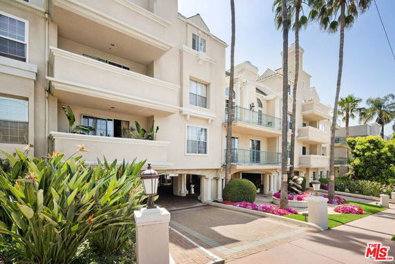 Front view of a multi-story residential building with balconies and a landscaped entrance.