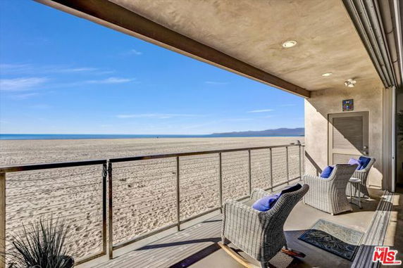 Panoramic view of a sandy beach from a balcony with wicker chairs.