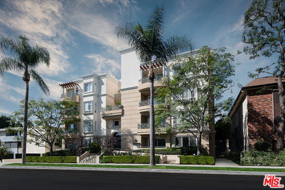 Front view of a multi-story apartment building with balconies and trees.