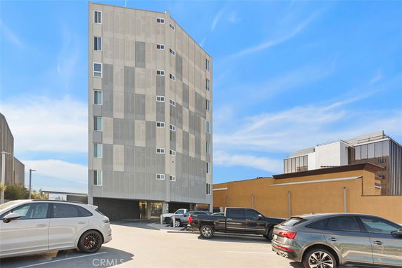 Front view of a multi-story building with a modern facade and adjacent parking area.