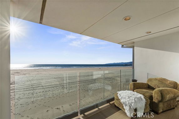 View of the beach and ocean from a balcony with glass railing.