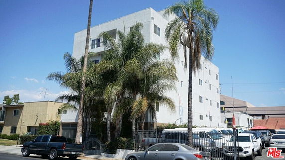 Front view of a multi-story apartment building with palm trees in front.