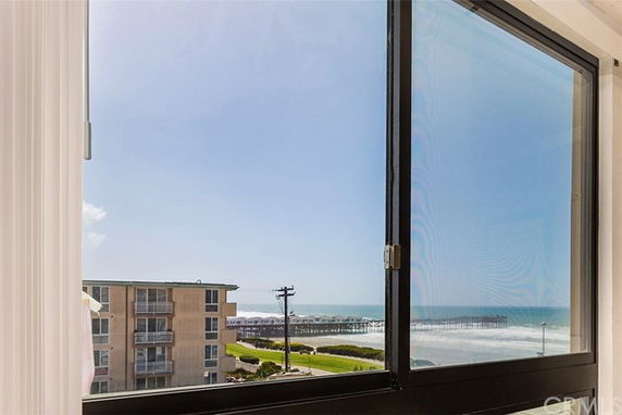 View of a beachfront apartment building with ocean and pier in the background seen through a window.