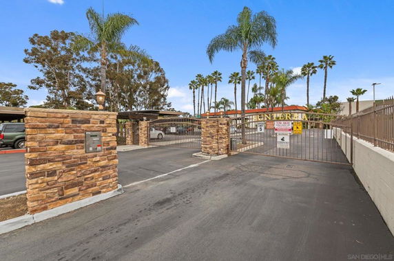 Gated entrance to a parking area with stone pillars and palm trees.