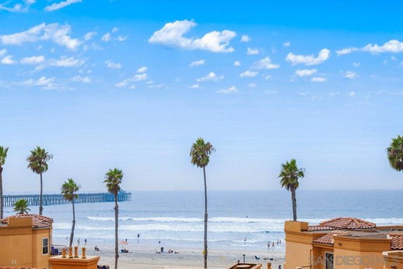 Panoramic view of a beach with palm trees and buildings along the shore.