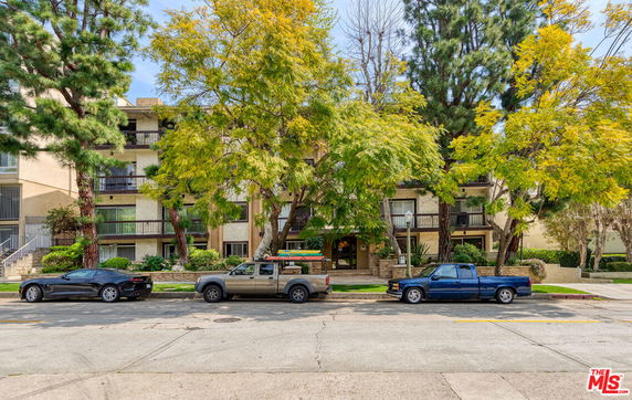 Front view of a multi-story residential building with balconies and surrounding trees.