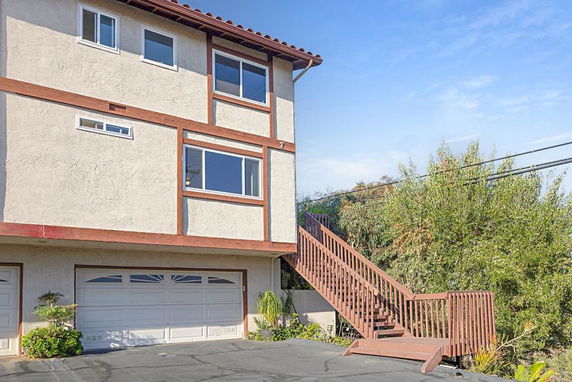 Side view of a multi-story building with a staircase leading to an upper level and double garage doors on the ground level.