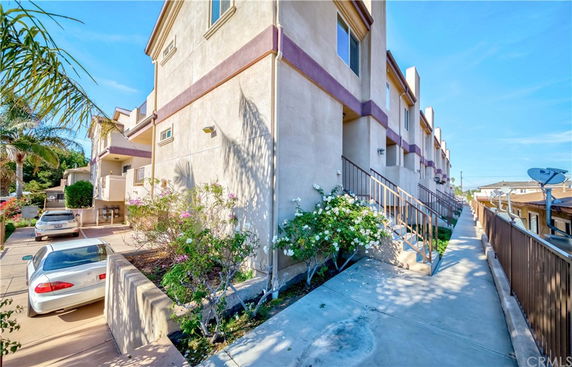 Side view of a multi-story townhouse with exterior stairs and nearby parked cars.
