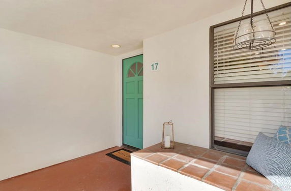 Front view of a house entrance with a turquoise door and a small seating area.