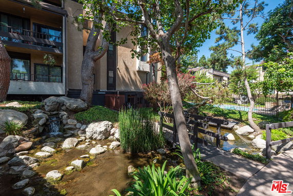 View of a building exterior with trees, rocks, and a small water feature.