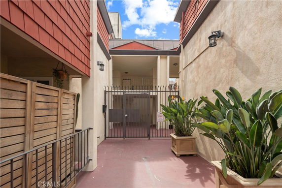 Entrance view of a building with red trim and gate, flanked by potted plants.