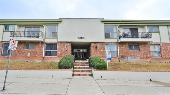 Front view of a multi-story residential building with balcony railings and brick facade.