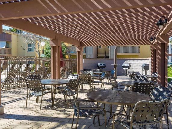 Outdoor seating area with a pergola and barbecue grills in a residential complex.