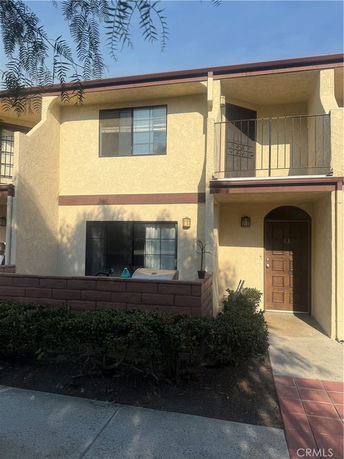 Front view of a two-story house with a small balcony and a brick-walled patio.