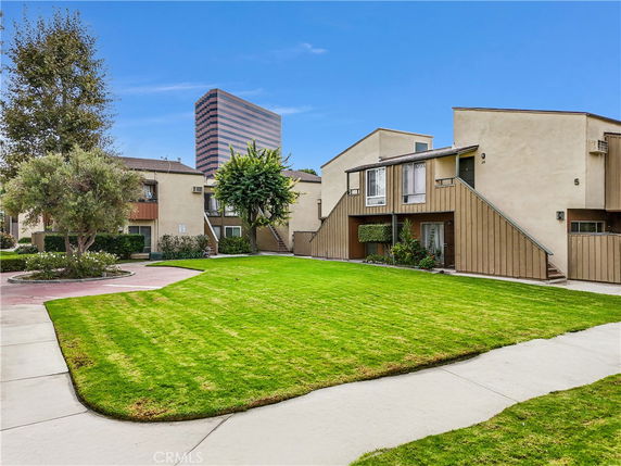 Front view of a multi-story residential building with outdoor stairs and surrounding green lawn.